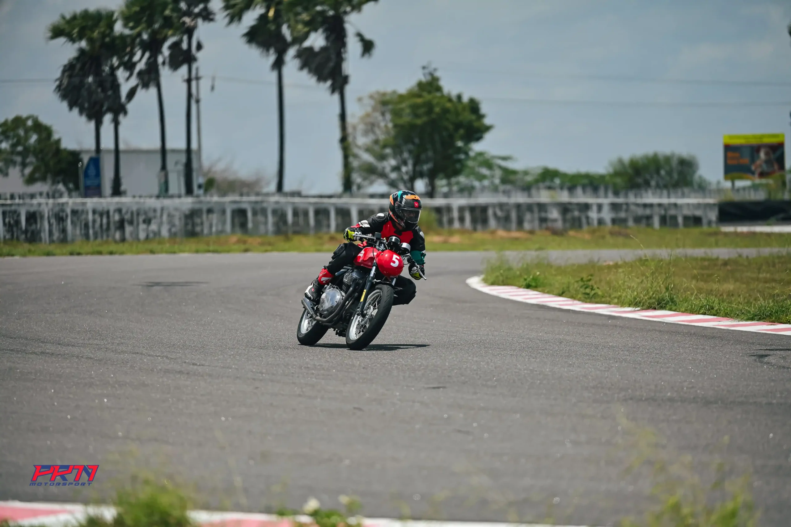 Motorcycle racer navigating a curve on a red Royal Enfield bike during a professional track training course, emphasizing advanced riding techniques.