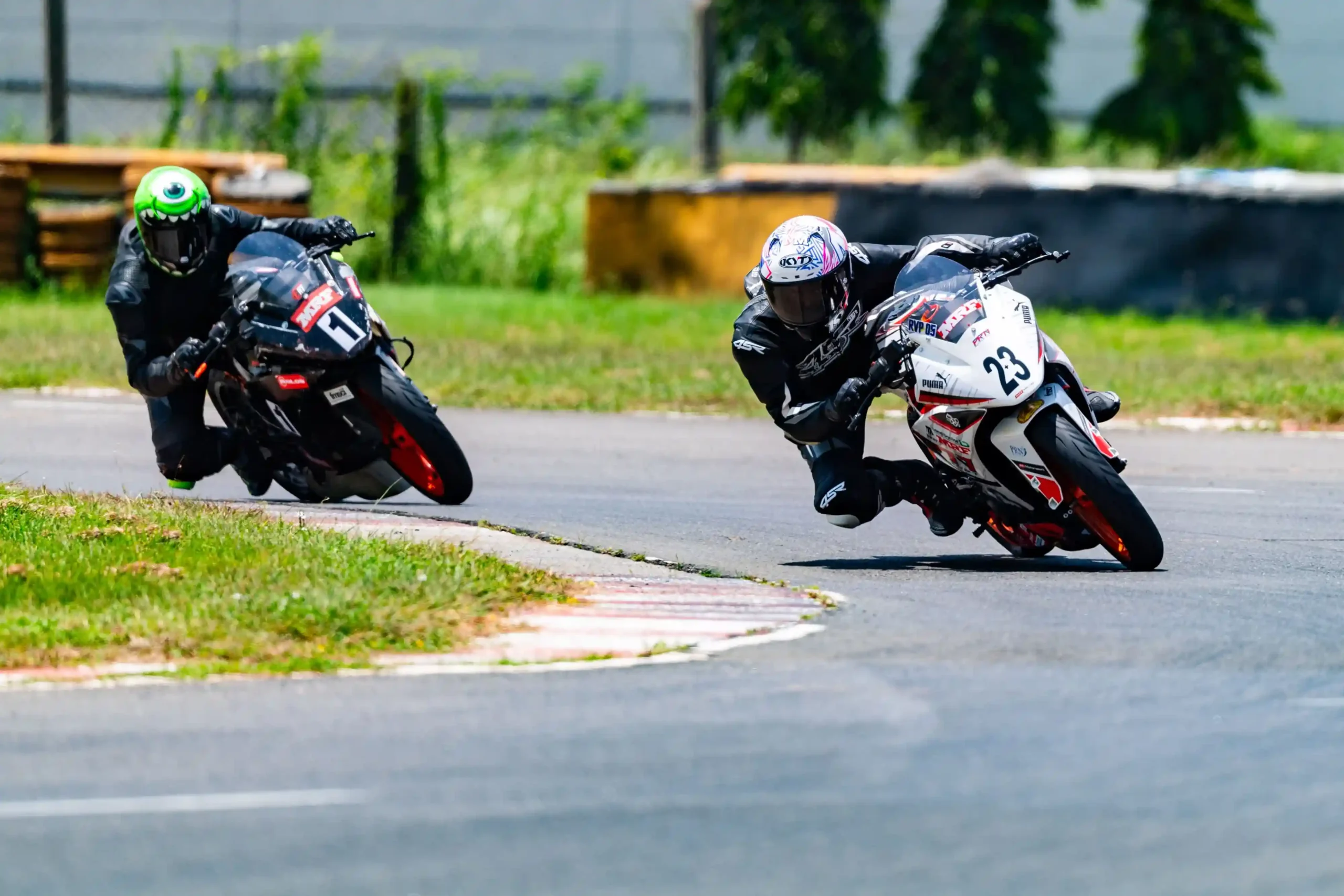 Showcasing the best GT track training school, two motorcycle racers lean into a curve on a track during a high-speed race, with vibrant green grass and a blurred background for emphasis.