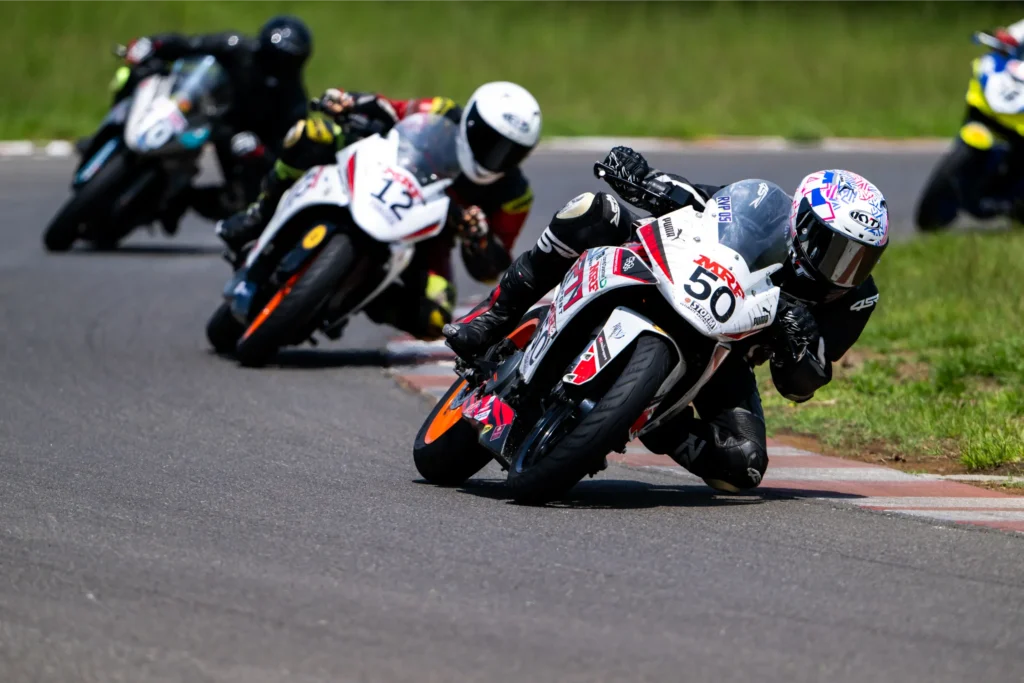 Motorcycle racers leaning into a sharp turn during a competitive track session, showcasing precision and speed during Level 1 GT track training.